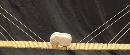 Testing a bridge made of paper drinking-straws and string, by using a stone elephant as a weight.